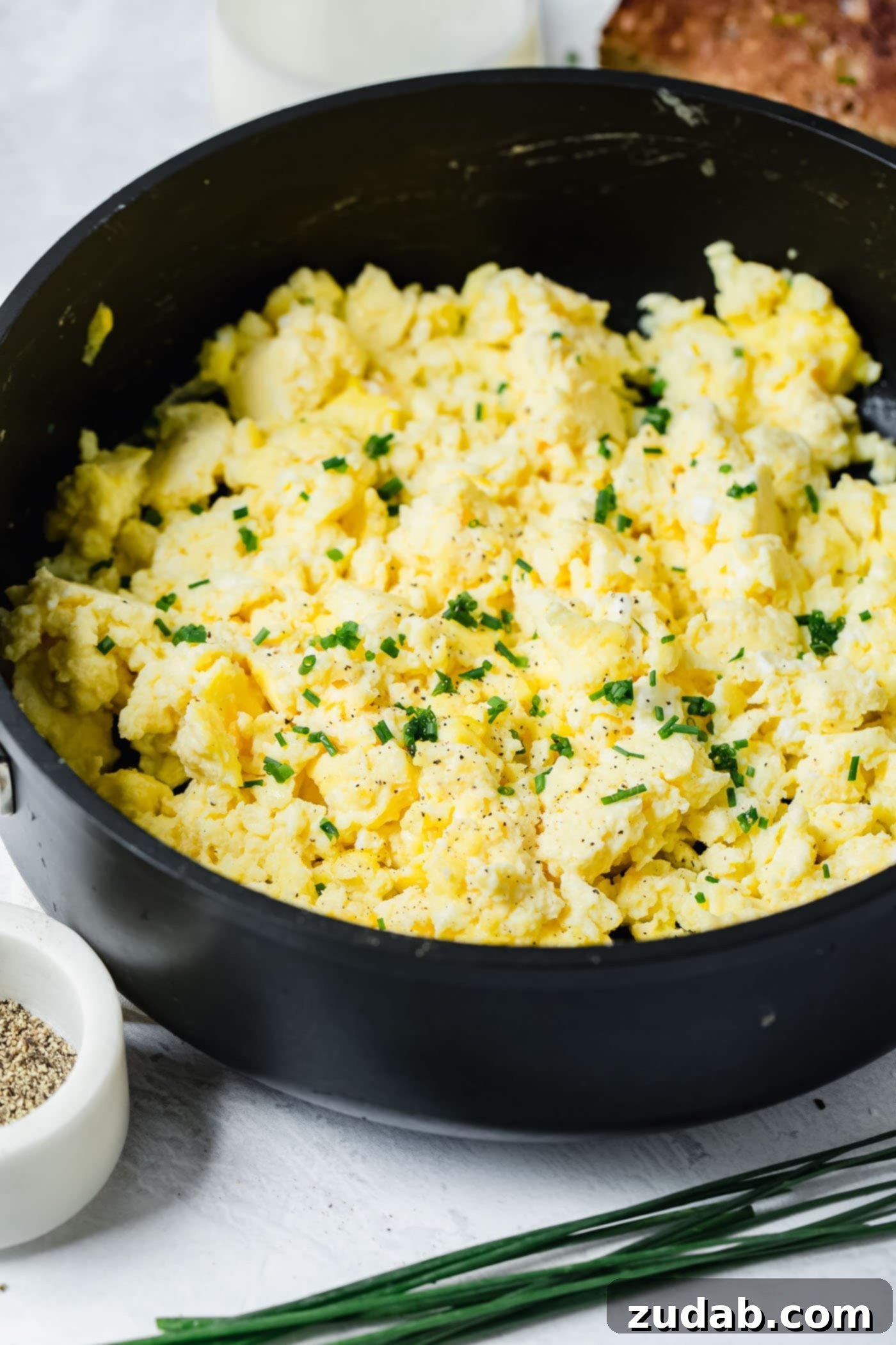 The Best Scrambled Eggs A black bowl filled with fluffy scrambled eggs sprinkled with slices of green onion.