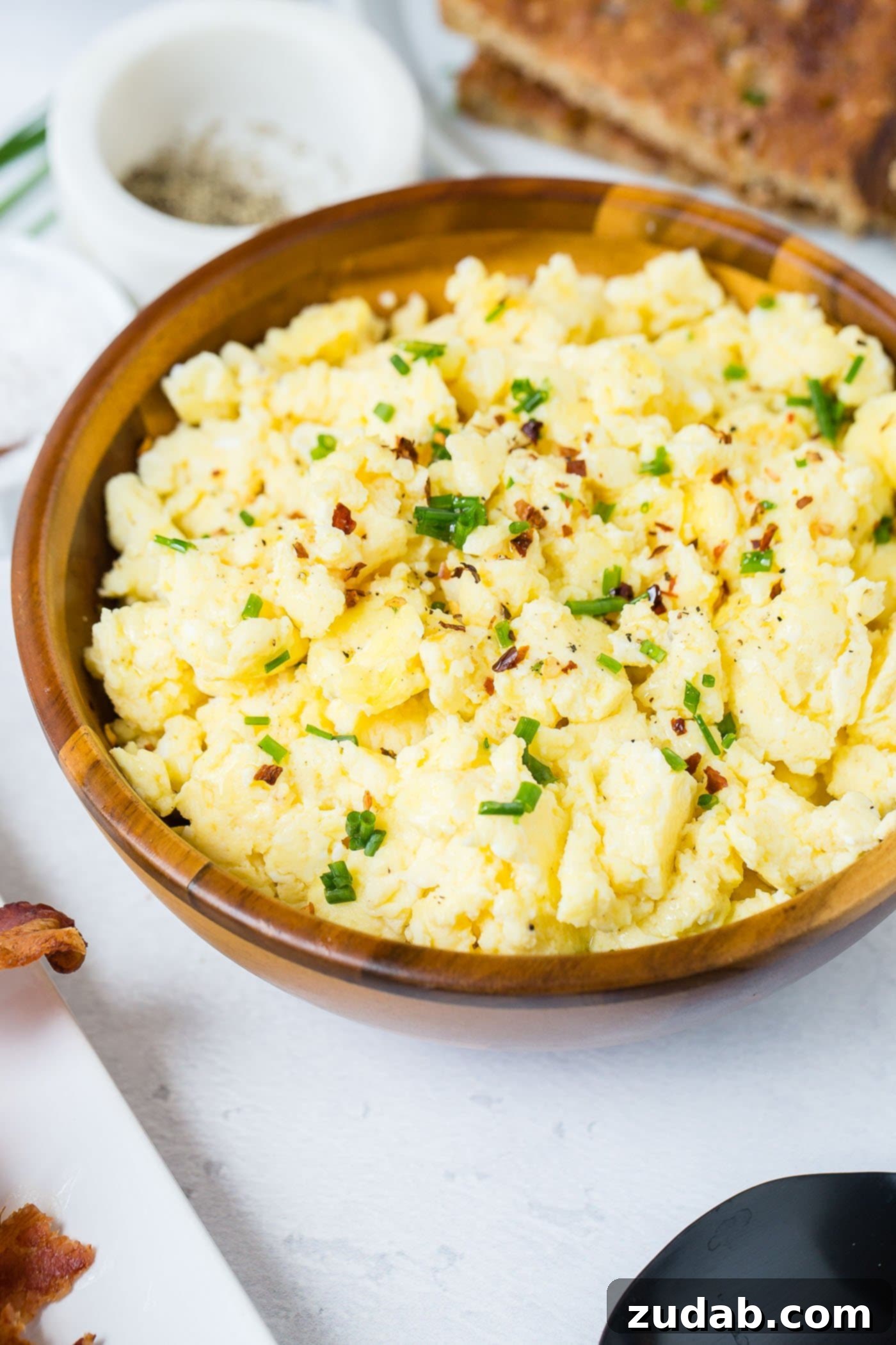 The Best Scrambled Eggs A wooden bowl of scrambled eggs. The eggs are sprinkled with fresh slices of green onion.