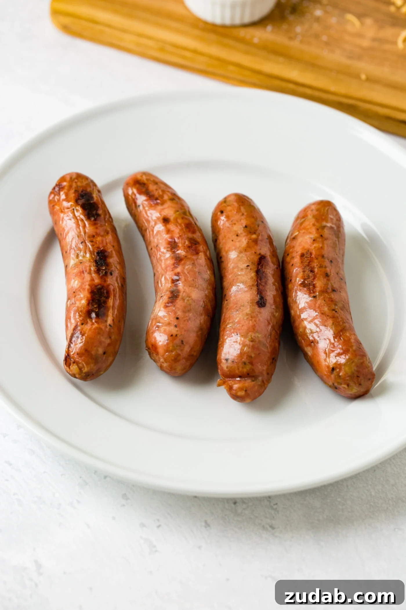 Spiced Apple Sausage Morning Wraps 3 Four apple chicken sausages on a white plate.
