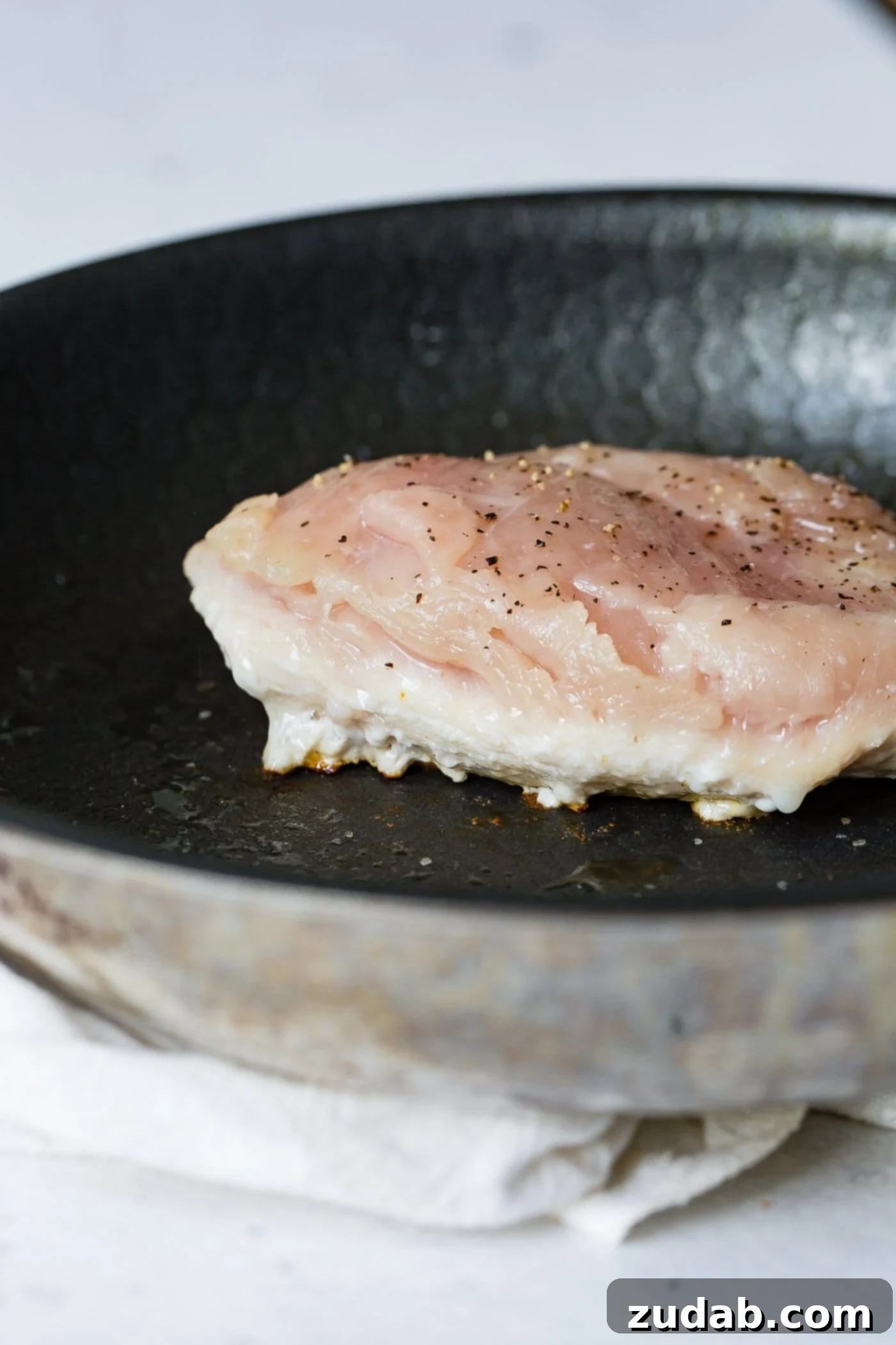 Perfectly Pan-Seared Chicken 2 A chicken breast cooking in a skillet. The breast is cooked about half way through.