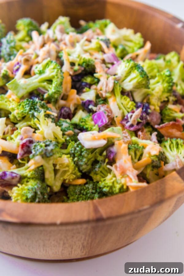 Everyone's favorite quick and easy side for our BEST broccoli salad recipe that's perfect for potlucks and BBQs. Plus it has bacon in it! golden raisins, craisins, sunflower seeds, bacon, frozen peas, red onion A close-up of a cold broccoli salad in a large bowl, showcasing the vibrant green broccoli, golden sunflower seeds, crispy bacon pieces, tender peas, and thinly sliced red onions, all coated in a rich, creamy dressing.