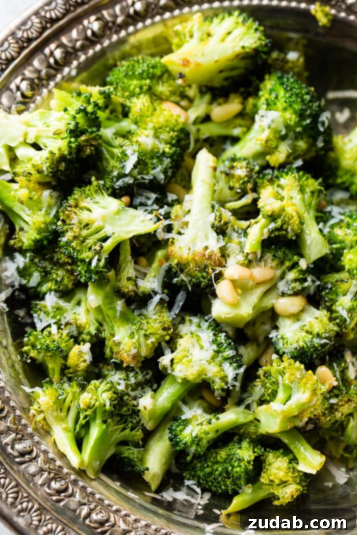 Bright Lemon Roasted Broccoli 2 A vintage silver bowl filled with glistening lemon roasted broccoli, topped with toasted pine nuts and grated Parmesan cheese, ready to be served as a delightful side dish.