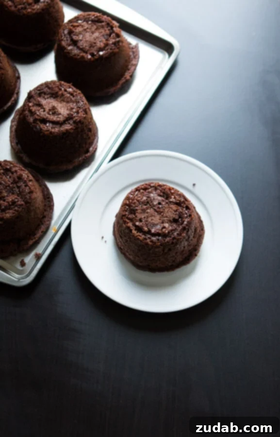 Copycat Chili's molten lava cakes recipe is way easier to make than you probably think and that hot fudge oozing out is such a crowd pleaser! A close-up of a freshly baked molten lava cake being drizzled with hot fudge, showcasing the process of filling the cake before reheating.