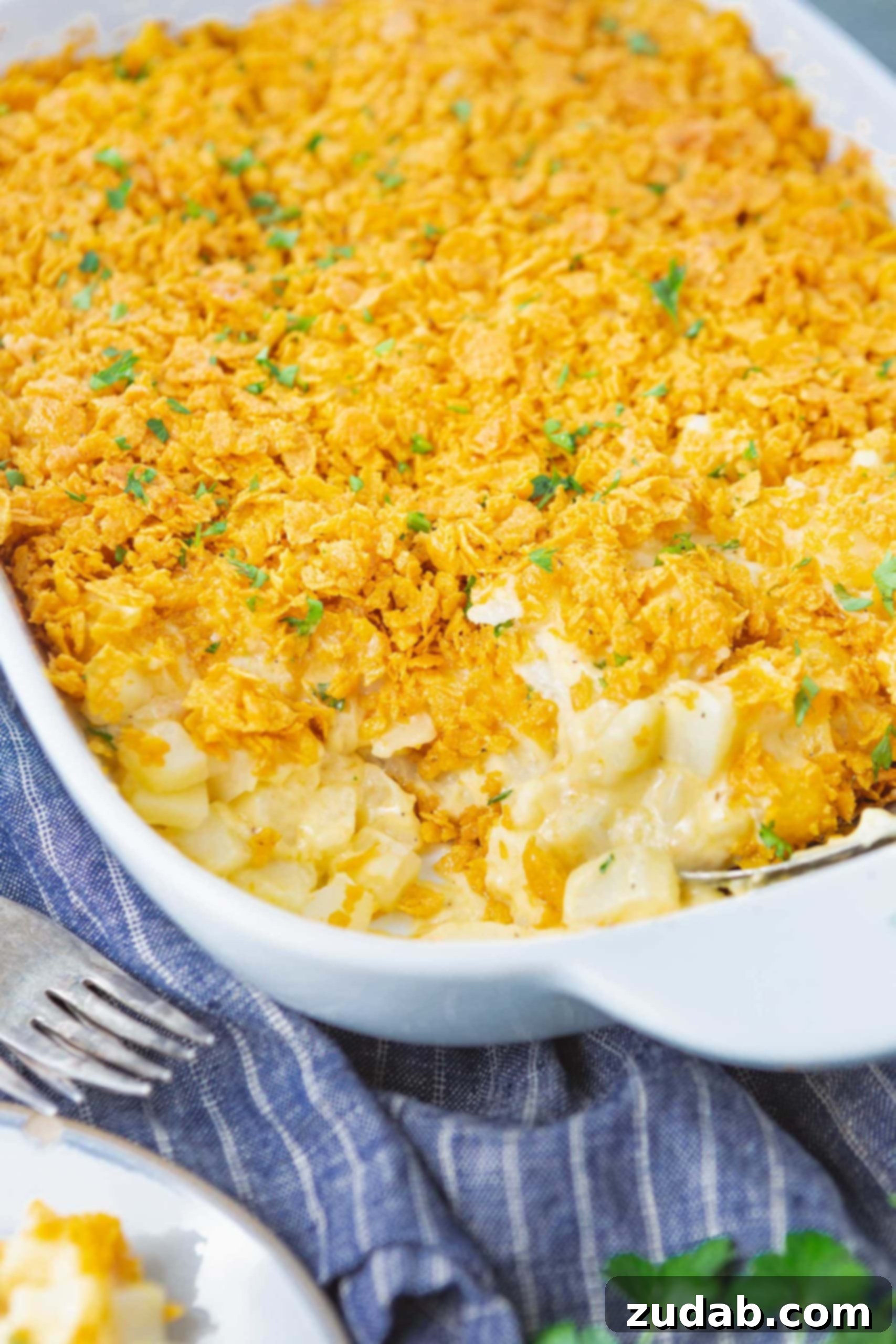Funeral Potatoes Cheesy Potato Casserole a photo of a casserole dish full of cheesy potato casserole with a serving in the corner of the dish removed.