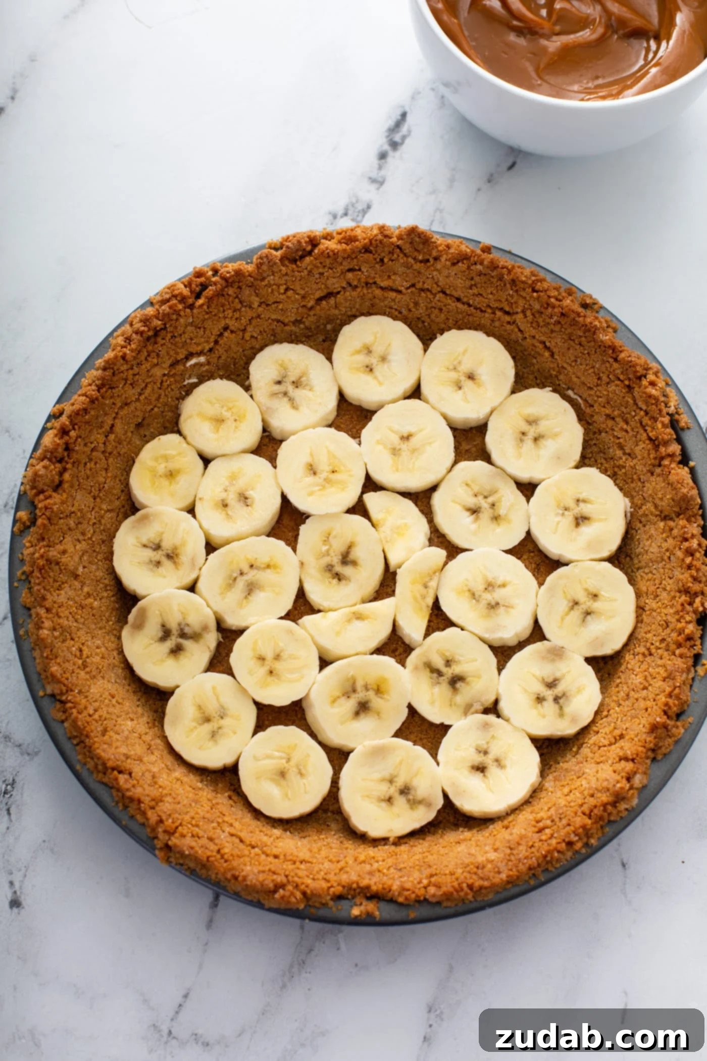 Decadent Dulce De Leche Banana Cream Pie 14 A graham cracker crust with sliced bananas covering the bottom of the crust.