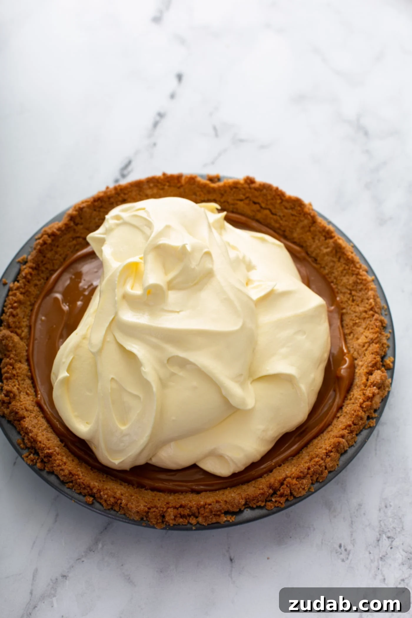Decadent Dulce De Leche Banana Cream Pie 16 A graham cracker crust filled with dulce de leche and banana cream filling that has been added, but not yet spread all over the dulce de leche.