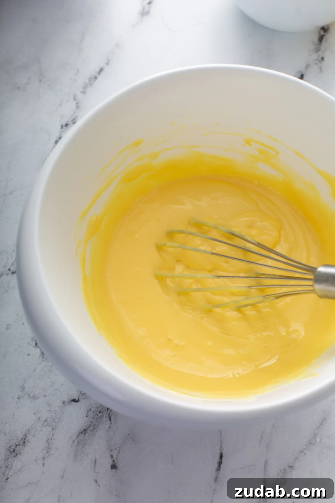Decadent Dulce De Leche Banana Cream Pie 10 A mixing bowl of pudding and cream cheese. The mixture is being whisked together to a creamy yellow consistency.