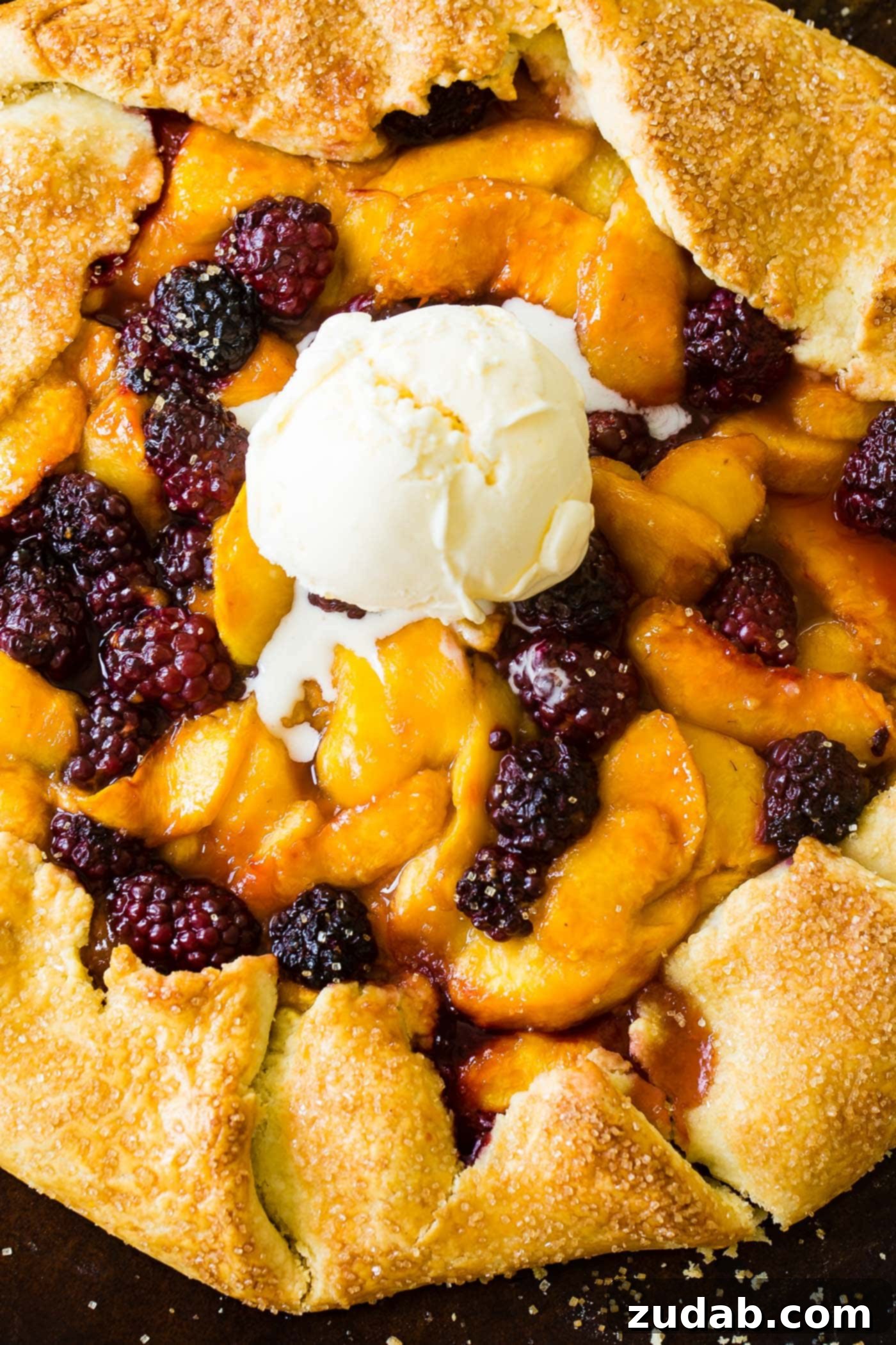 A rustic peach and blackberry galette cooling on a wire rack. The golden crust is folded imperfectly around a vibrant, bubbling fruit filling, creating an inviting homemade aesthetic. Scattered sugar crystals glisten on the crust. It's truly a beautiful dessert.