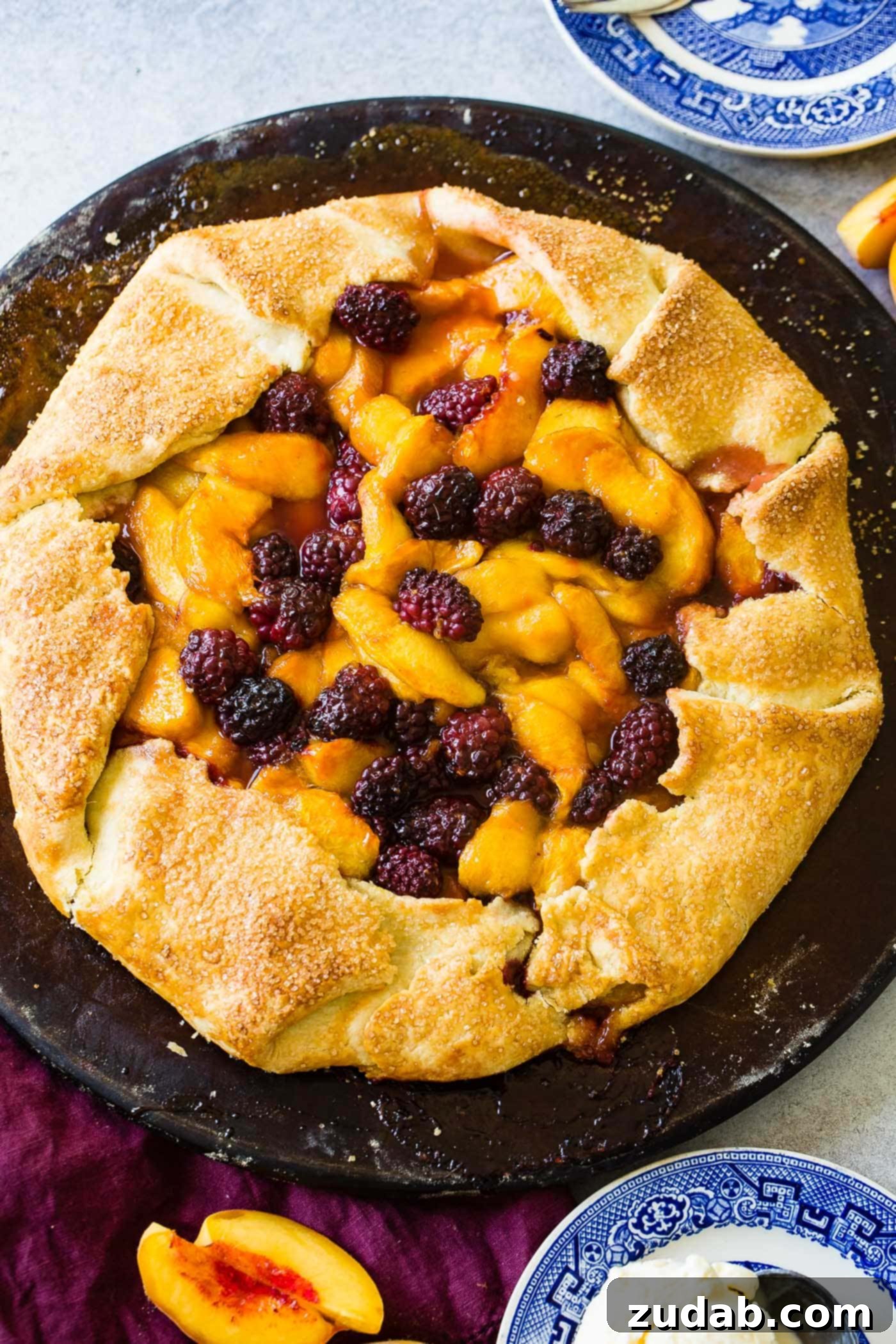 A close-up of a partially baked peach blackberry galette, showing the golden-brown, rustic crust folded around the vibrant, juicy fruit filling. The peaches are soft and slightly caramelized, while the blackberries retain their shape, creating an appealing texture contrast.