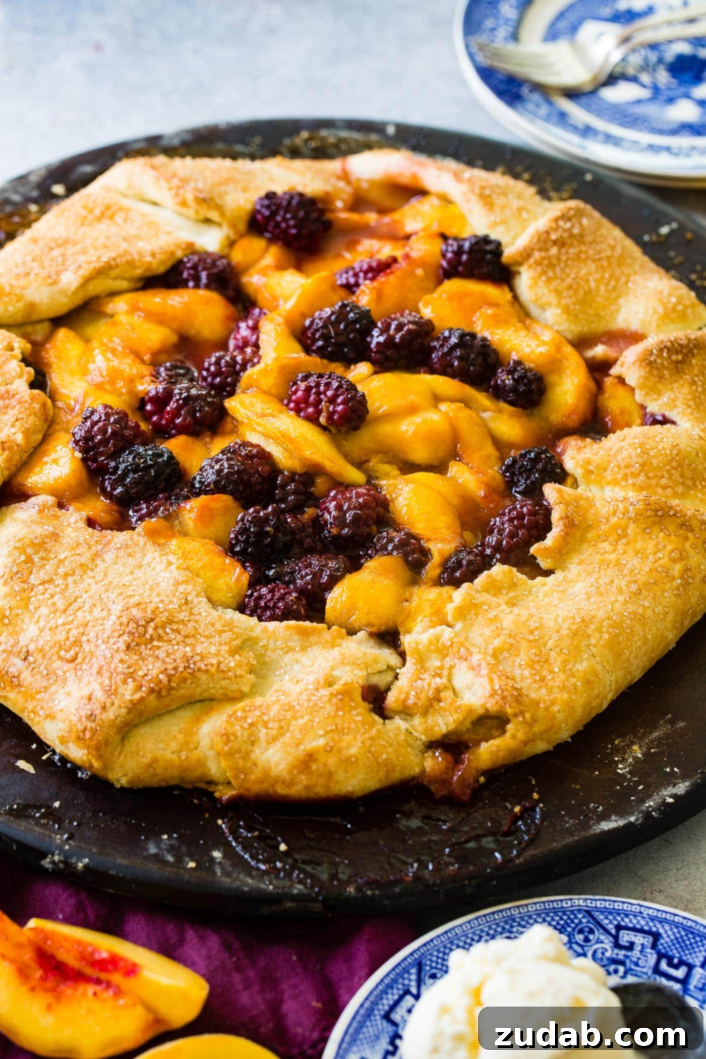Another overhead shot of a baked peach blackberry galette. The crust is artfully folded, showcasing the generous fruit filling with hints of the golden, flaky pastry. The colors of the peaches and blackberries are vibrant, suggesting freshness and deliciousness.