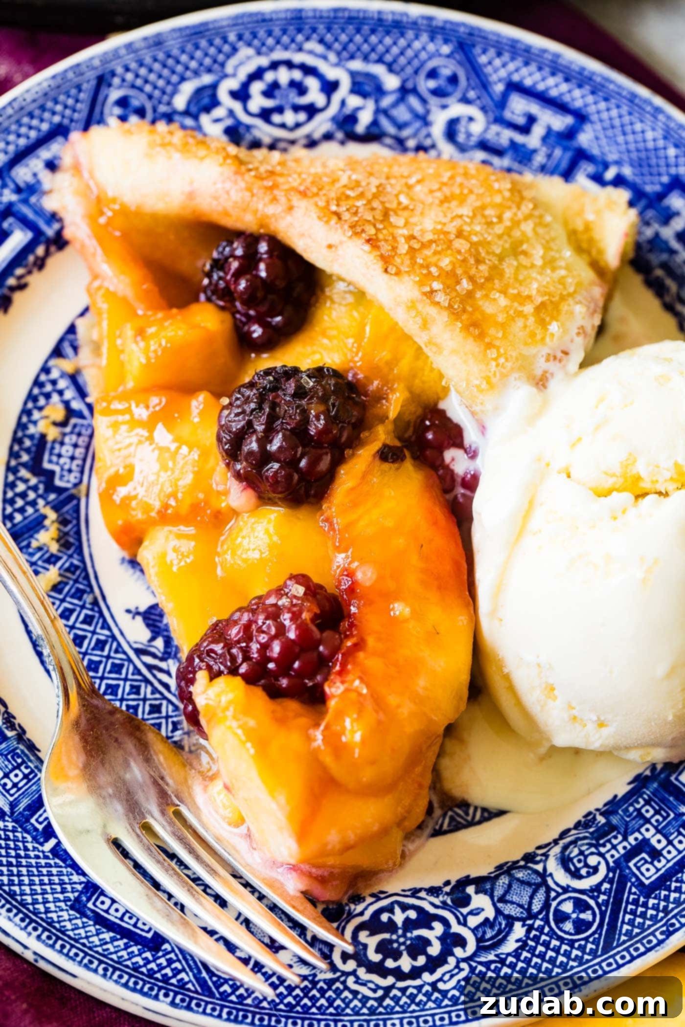 The full peach blackberry galette on a parchment-lined baking sheet. The entire rustic dessert is presented, highlighting the rich fruit filling, the golden crust, and the overall inviting homemade appearance, ready to be sliced and served.