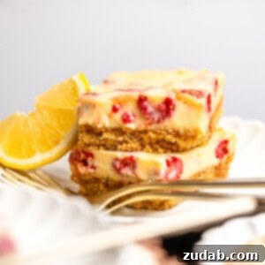 Tangy Lemon Raspberry Bars 2 a photo of two creamy lemon raspberry bars with graham cracker crust stacked on each other on a small dessert plate with a lemon wedge next to them