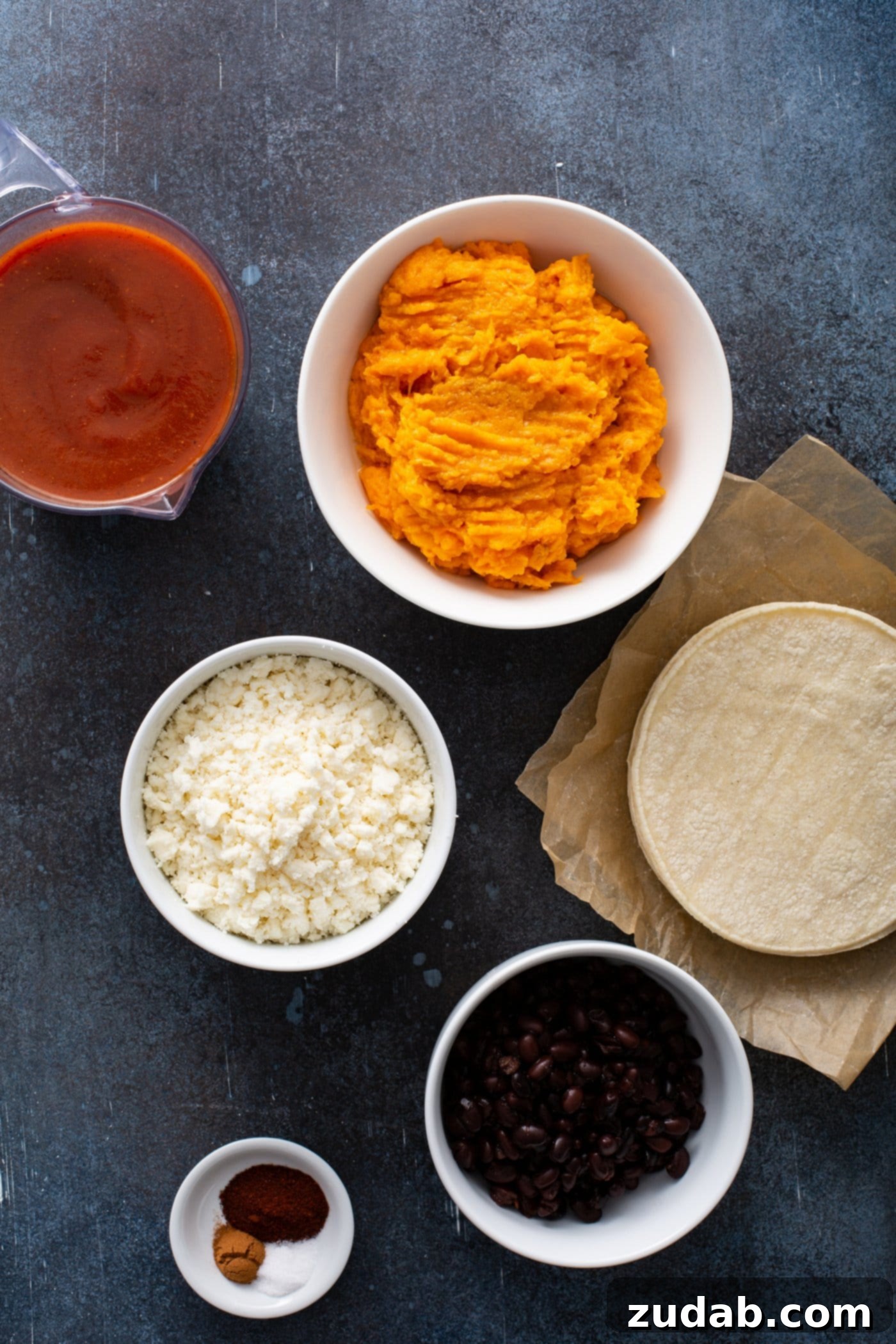 Small containers of mashed sweet potato, red enchiladas sauce, queso fresco cheese, and corn tortillas.
