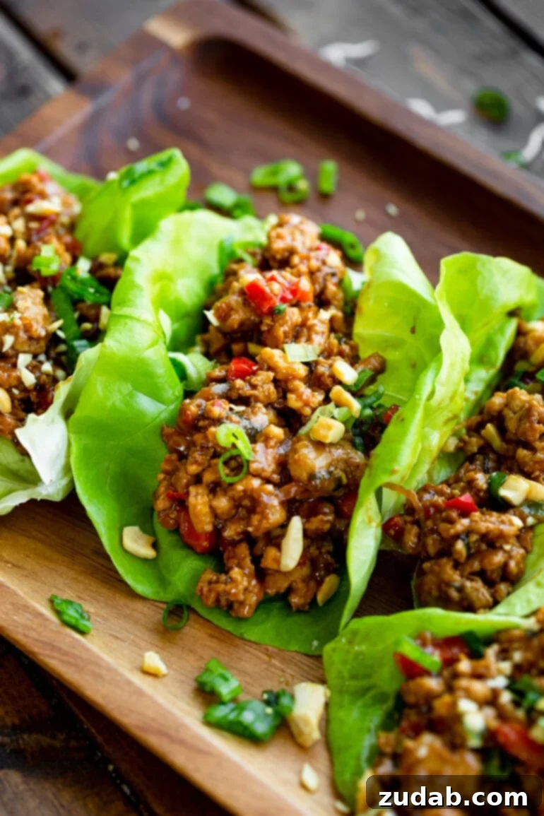 A vibrant close-up of fresh, crisp butter lettuce leaves filled with a rich Thai peanut turkey mixture, garnished with sliced green onions and slivered almonds.