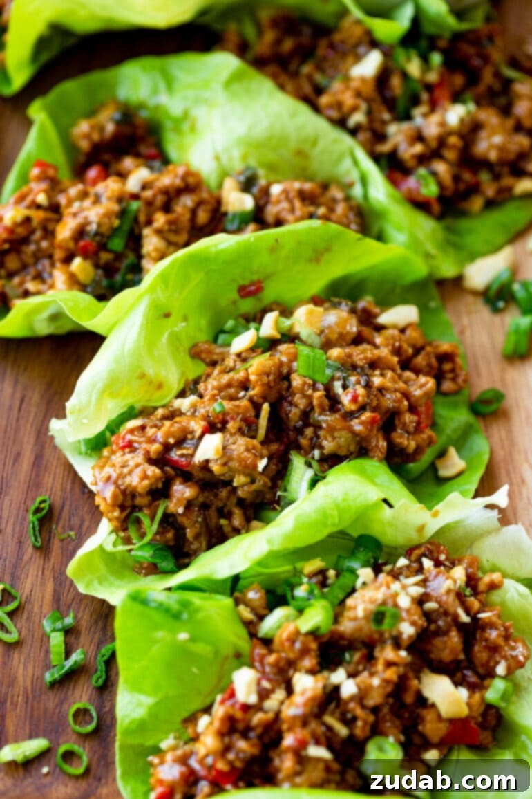 A close-up shot of several beautiful lettuce wraps, overflowing with juicy, saucy minced turkey and topped generously with fresh sliced green onions.