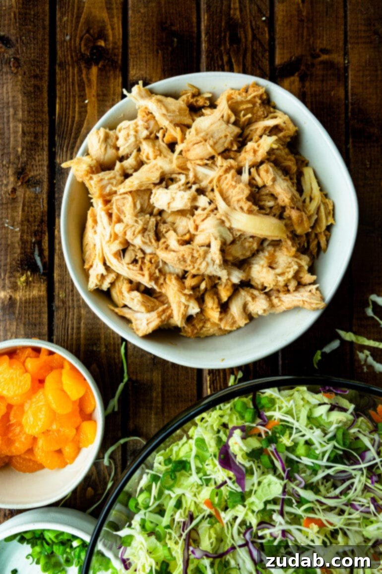a photo of a bowl full of shredded cooked chicken sitting next to a bowl of shredded cabbage and a small bowl of mandarin oranges.