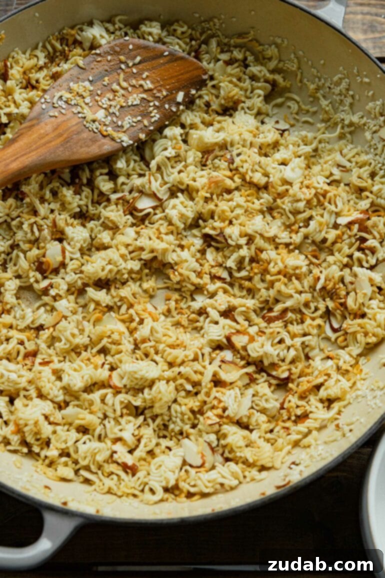 a photo of crushed up ramen noodles being toasted in a shallow dutch oven.