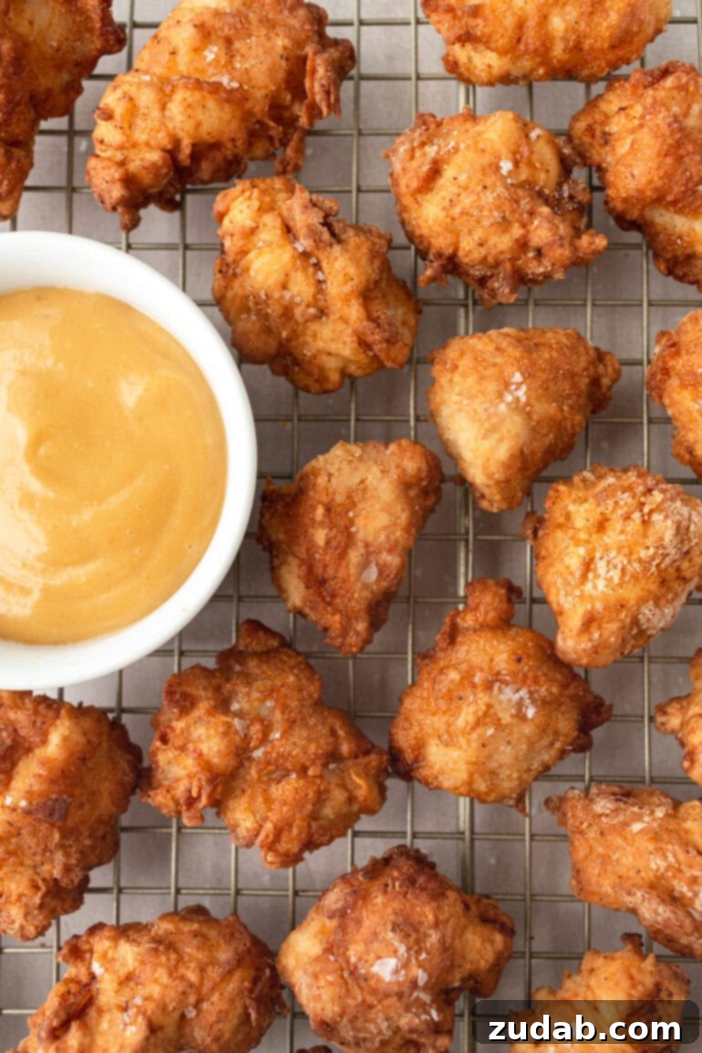A photo of several golden crispy homemade Chick-fil-A nuggets sitting on a wire cooling rack with a small bowl of dipping sauce next to them.