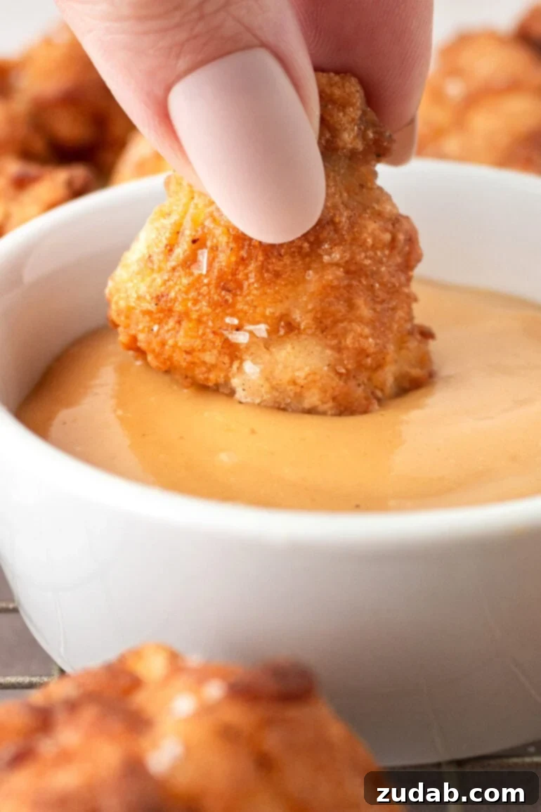 A photo of someone dipping a crispy golden homemade chicken nugget in an orange dipping sauce.