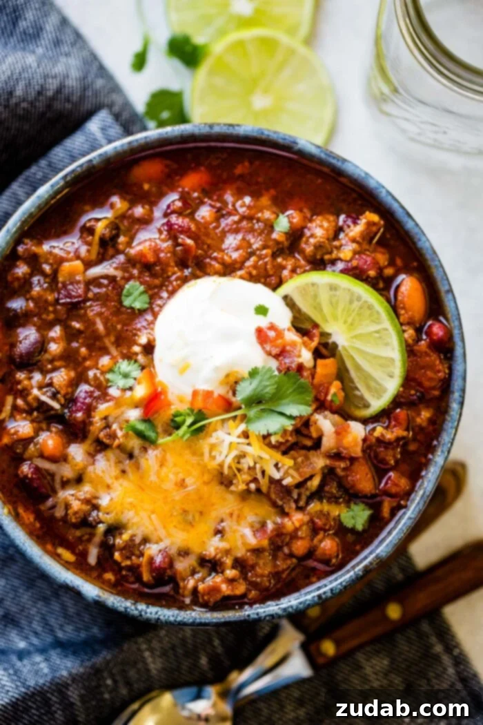a photo of a large bowl full of chili topped with cheese, sour cream, cilantro, bacon bits and a slice of fresh lime.