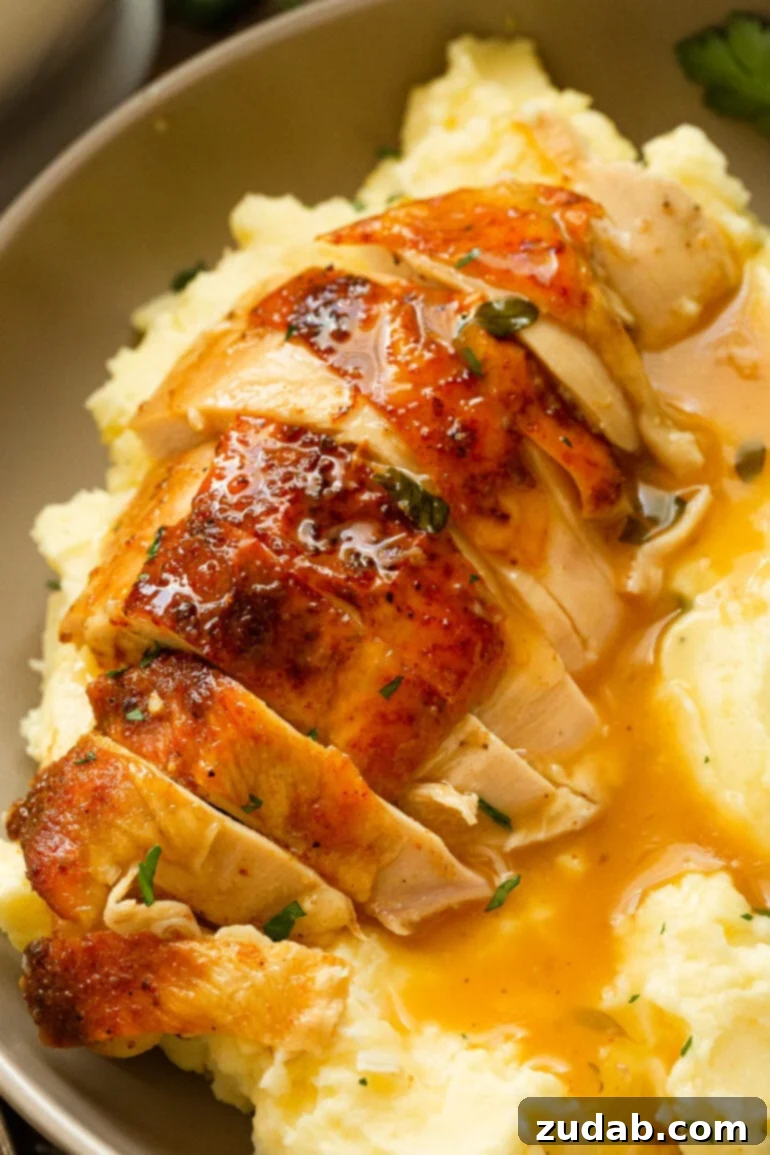 Irresistible Honey Roasted Chicken 2 A glistening golden honey roasted chicken breast, expertly sliced and served atop a bed of creamy mashed potatoes, generously draped with rich gravy.