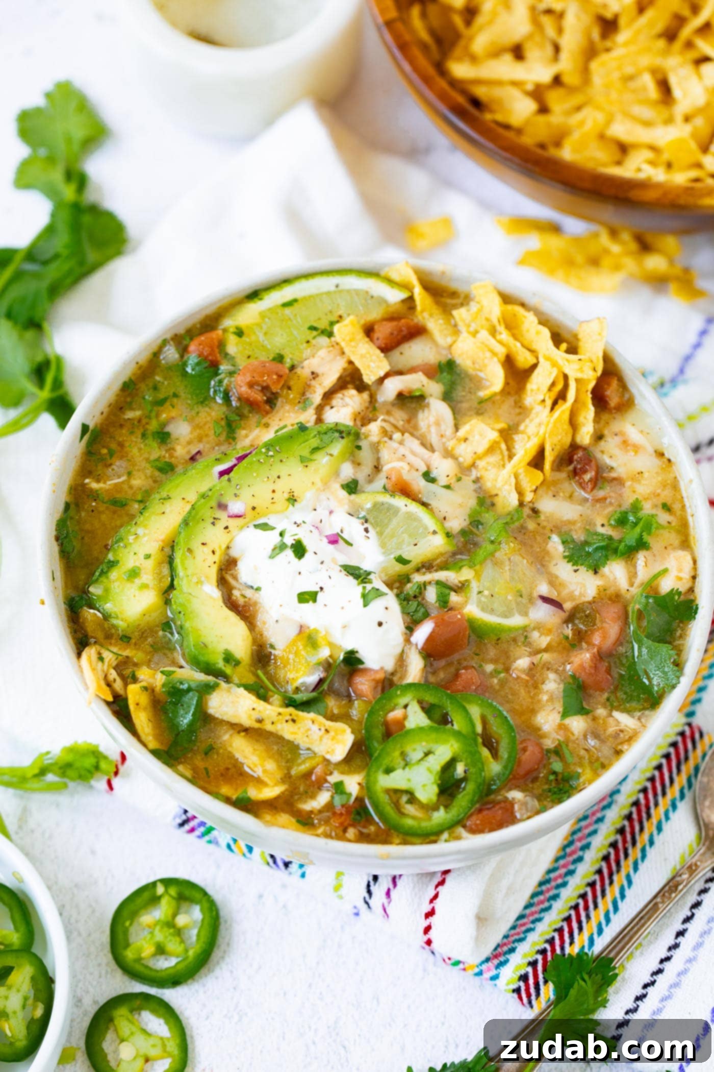 Delicious bowl of white chicken chili topped with sour cream, avocado, tortilla strips, and fresh jalapeno slices.