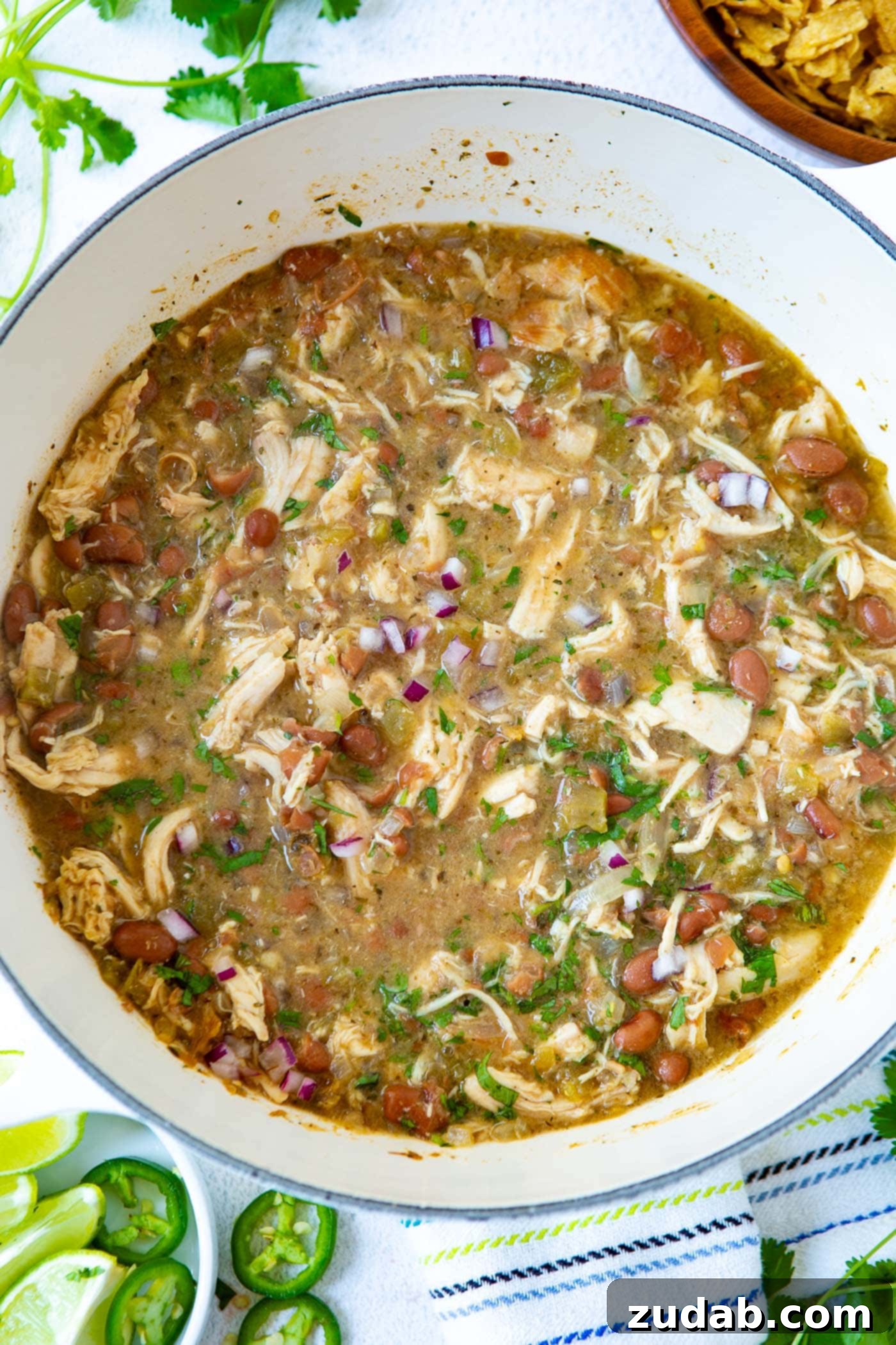A pot filled with hearty white chicken chili, featuring shredded rotisserie chicken, pinto beans, diced red onions, and fresh cilantro.