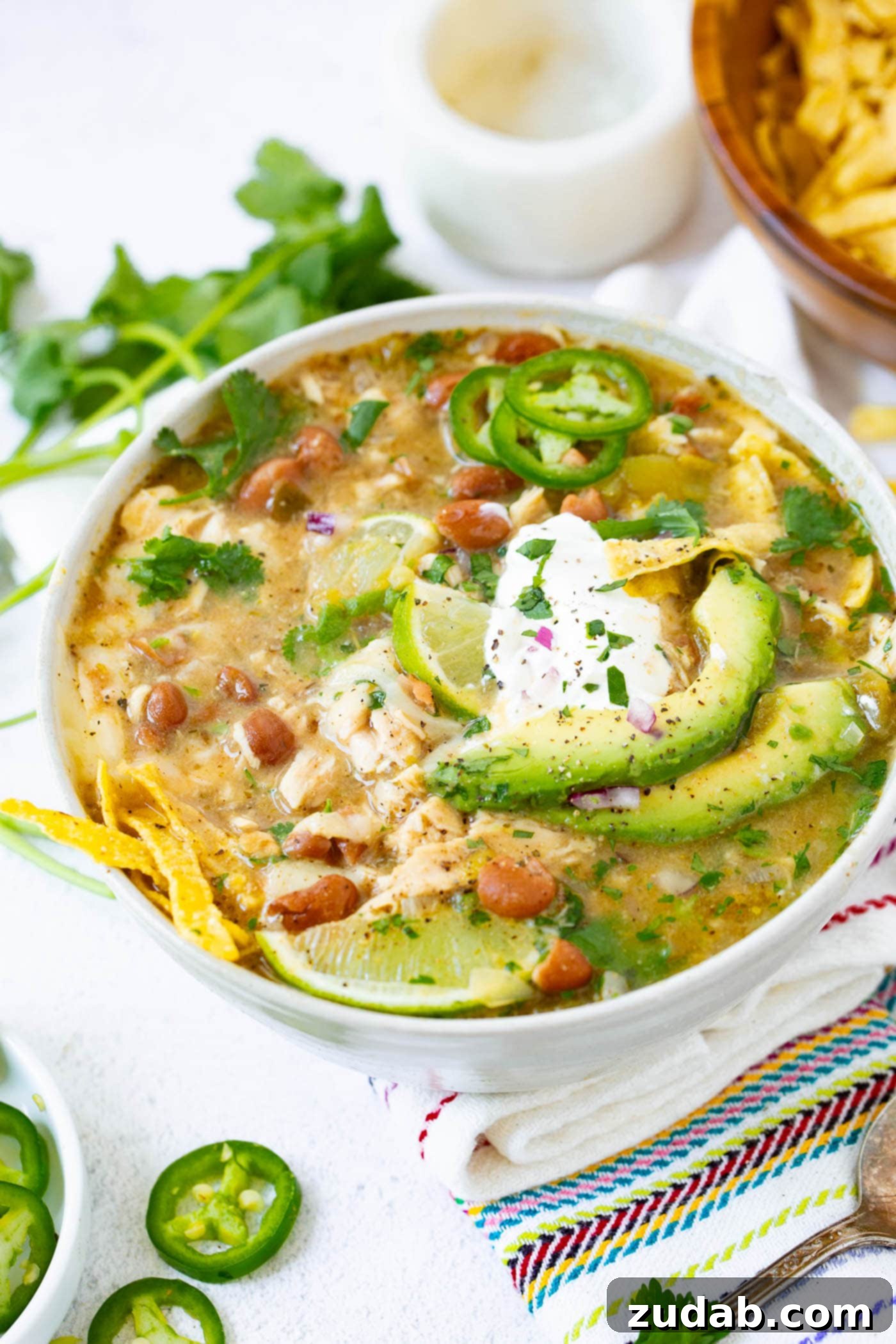 Cozy bowl of white chicken chili, perfect for comfort, topped with sour cream, avocado, tortilla strips, and fresh jalapeno slices.