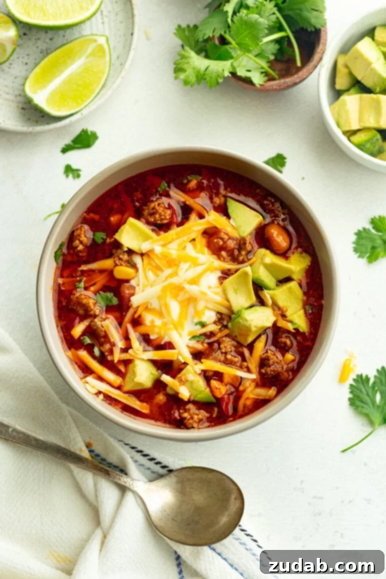 Easy Instant Pot Taco Soup 5 A grey bowl filled with mexican sopa, finished with fresh cilantro, creamy sour cream, shredded cheese, and avocado pieces, sitting on a wooden table.