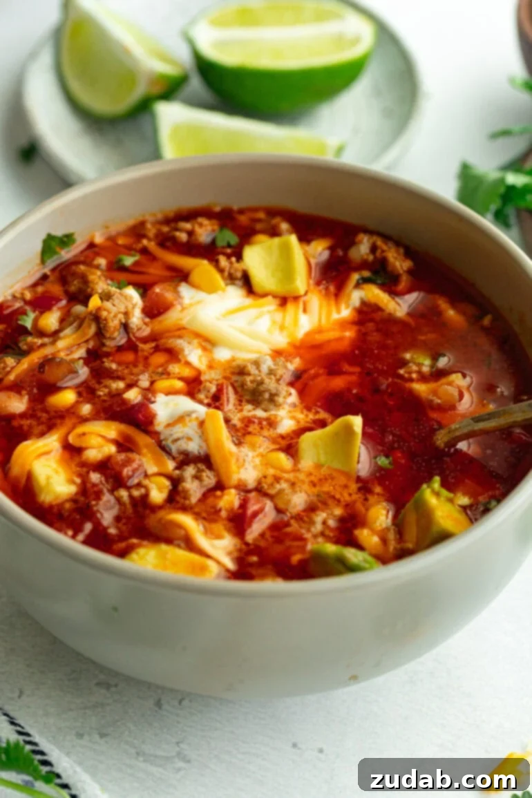 Easy Instant Pot Taco Soup 6 Grey bowl of Instant Pot taco soup on a white countertop, adorned with fresh cilantro, sour cream, shredded cheese, and sliced avocado.