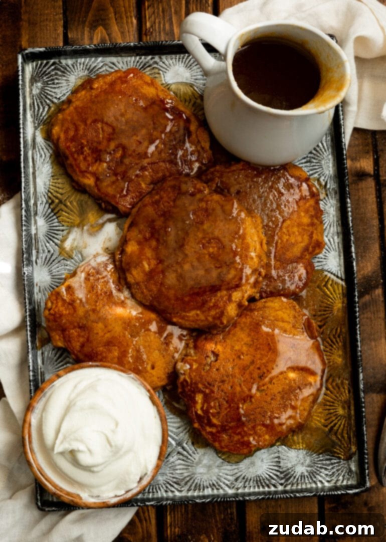 Homemade Whole Wheat Pumpkin Pancakes with Cinnamon Caramel Syrup 5 An overhead shot of a baking sheet filled with golden whole wheat pumpkin pancakes, lavishly covered in cinnamon caramel syrup, with a small bowl of whipped cream in the corner.