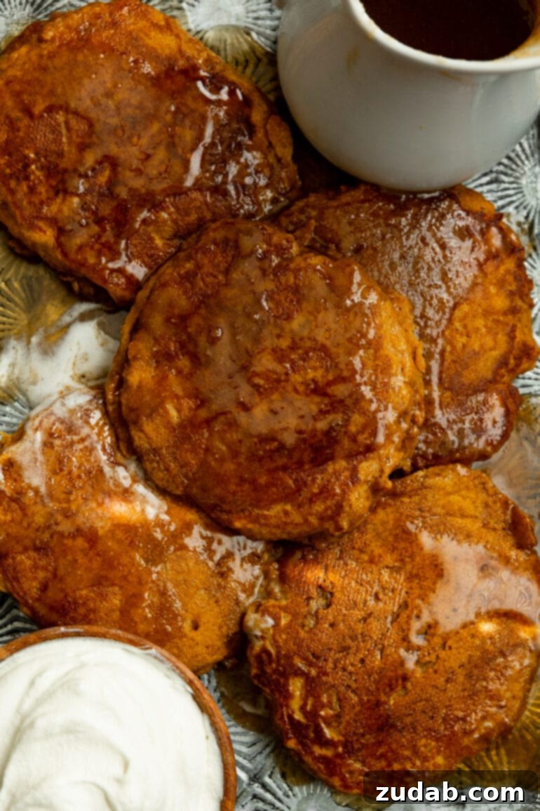 Homemade Whole Wheat Pumpkin Pancakes with Cinnamon Caramel Syrup 7 A comforting scene featuring several golden pumpkin pancakes arranged on a baking sheet, generously coated with cinnamon caramel syrup. A bowl of fluffy whipped cream and a carafe of extra syrup complete the enticing breakfast spread.
