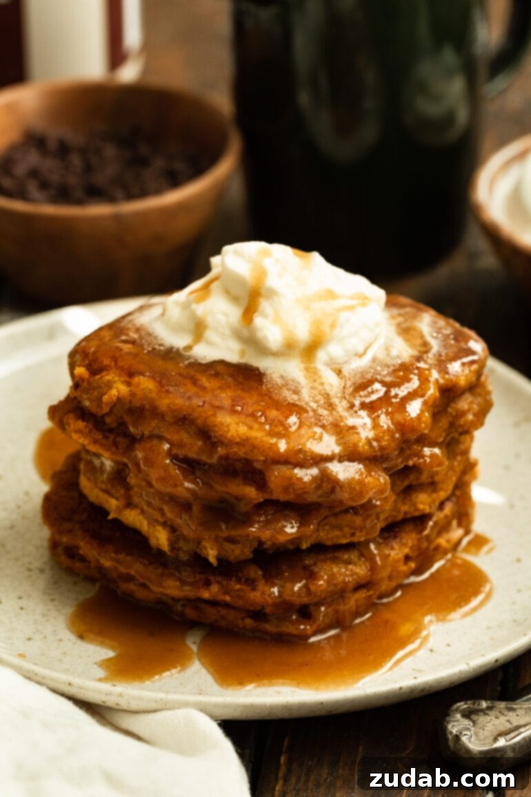 Homemade Whole Wheat Pumpkin Pancakes with Cinnamon Caramel Syrup 8 A stunning stack of whole wheat pumpkin pancakes resting on a pristine white plate, generously adorned with glistening cinnamon caramel syrup and a dollop of melting butter.