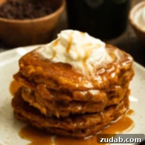 A photo of a stack of whole wheat pumpkin pancakes sitting on a white plate topped with cinnamon caramel syrup and a dollop of melting butter