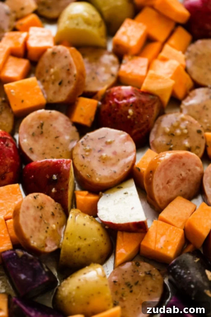 Sticky Honey Garlic Kielbasa Skillet 3 Uncooked Kielbasa slices, sweet potatoes, and mixed potatoes spread on a sheet pan, seasoned and ready for roasting.