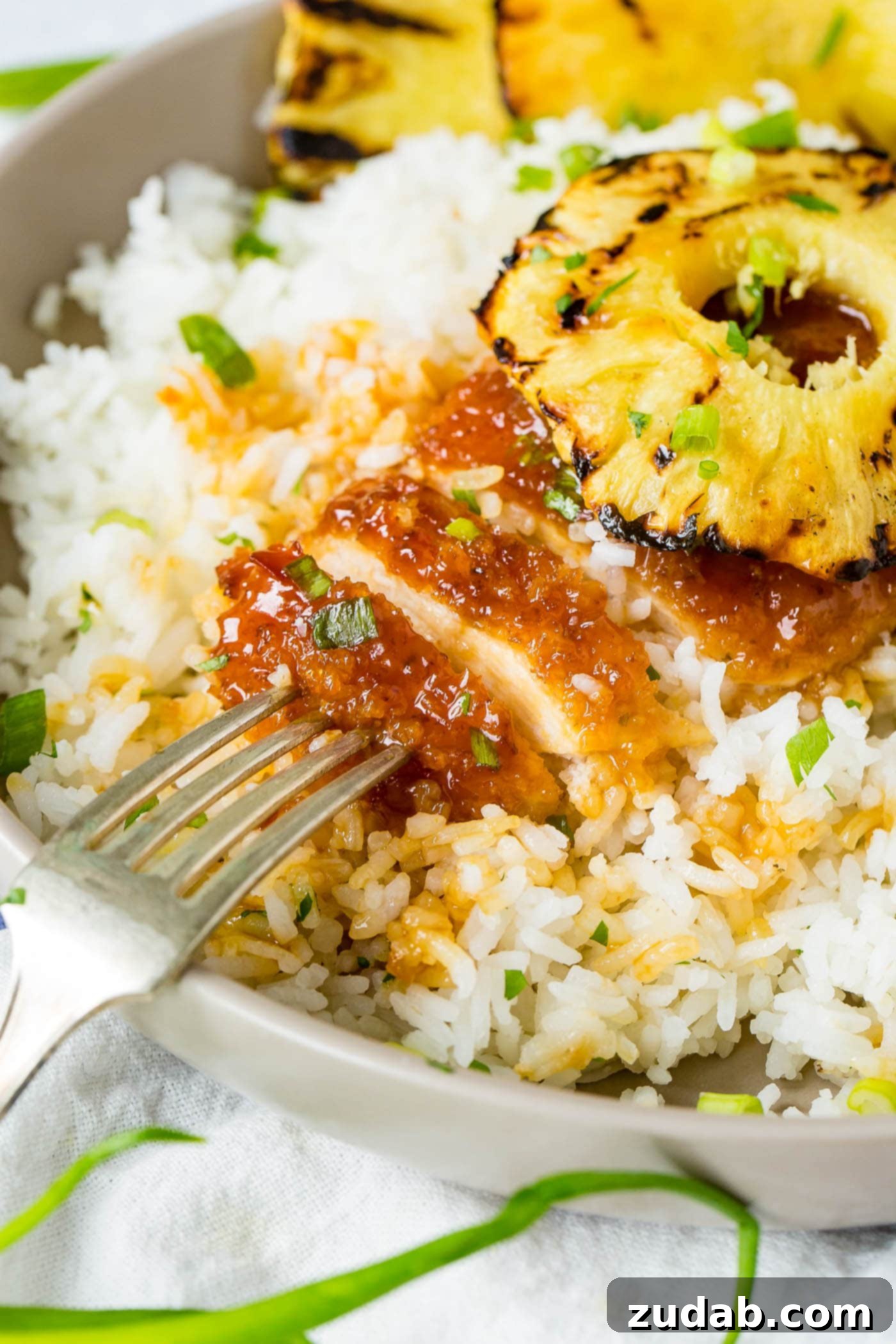 Speedy Sweet & Sour Pineapple Chicken 7 A bowl of white rice topped with breaded chicken sticky sauce chicken like sweet and sour sauce then a beautiful piece of grilled pineapple on top, illustrating an easy and flavorful dinner