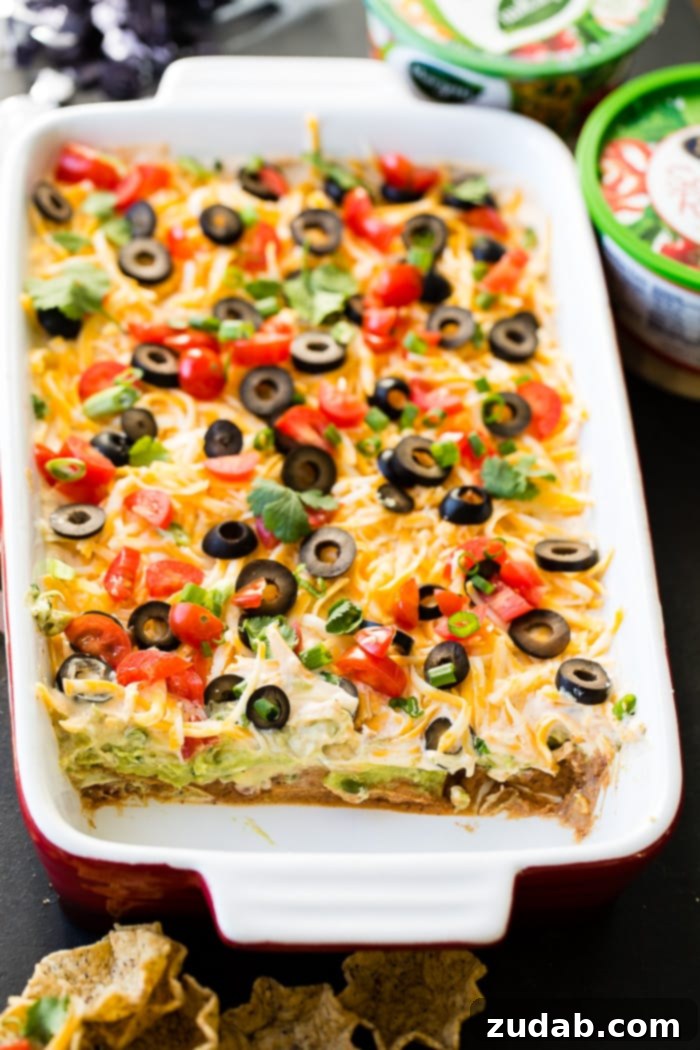 Ultimate Fiesta 7-Layer Dip 6 A large, inviting baking dish brimming with homemade Mexican 7 Layer Dip, topped with a colorful array of fresh ingredients including cheese, tomatoes, olives, green onions, and cilantro.