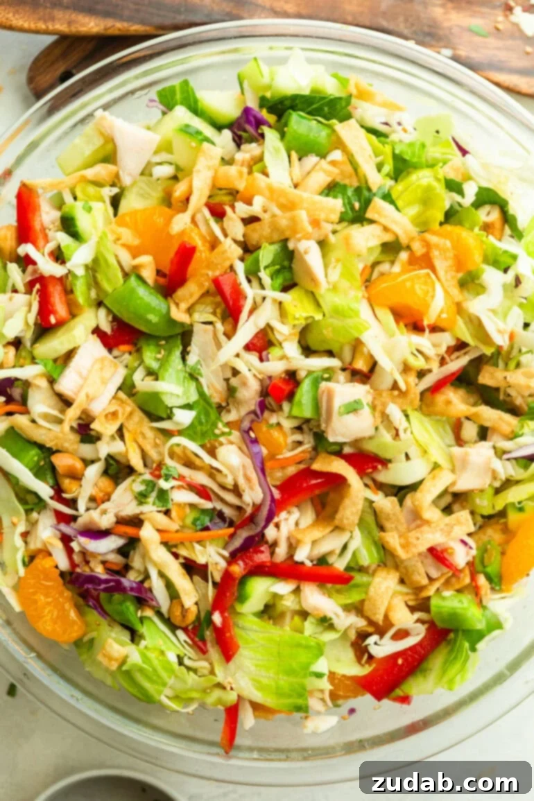 Crispy Wonton Chicken Salad 2 a large glass bowl full of wonton chicken salad with shredded cabbage, mandarin oranges. sliced red peppers and wonton strips, brightly lit and ready to serve