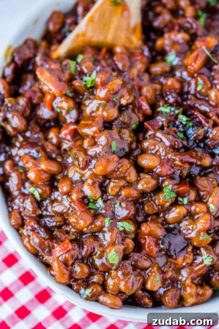 A white bowl full of saucy baked beans with chopped cilantro sitting on a red checkered napkin 
