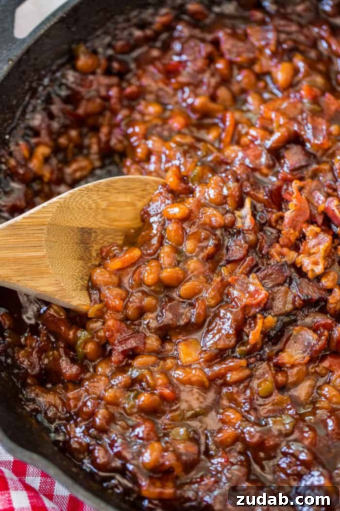 A cast iron skillet with saucy baked beans and a wooden spoon
