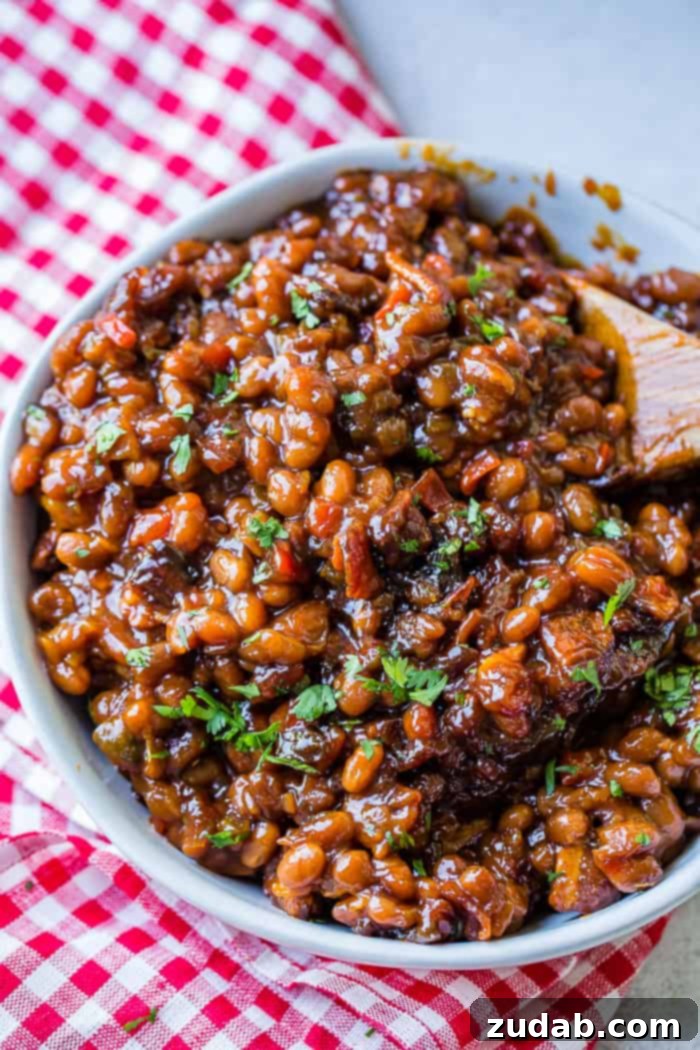 A white bowl full of saucy baked beans with chopped cilantro sitting on a red checkered napkin 