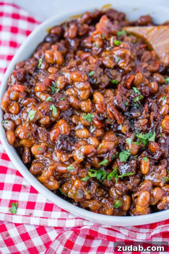 A white bowl full of a saucy homemade BBQ side with chopped cilantro sitting on a red checkered napkin 