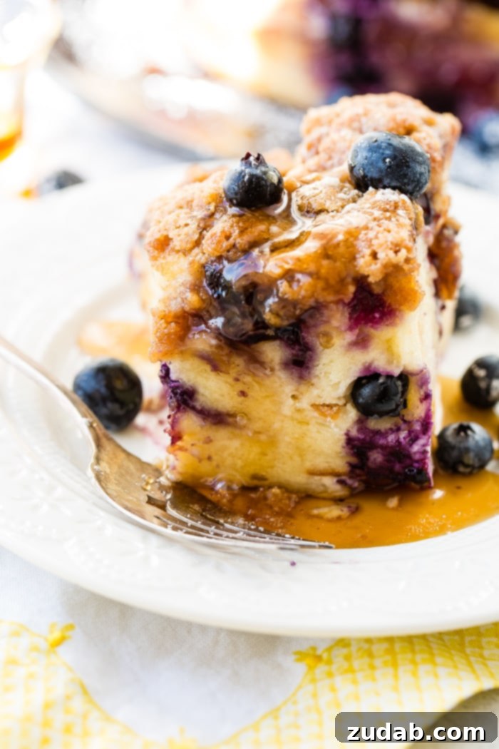3 Irresistible Instant Pot Blueberry French Toast Bakes 5 Blueberries scattered on a piece of French toast bake, topped with maple syrup and powdered sugar, served for breakfast or brunch. A vintage fork rests on a white lace plate, creating an inviting scene.