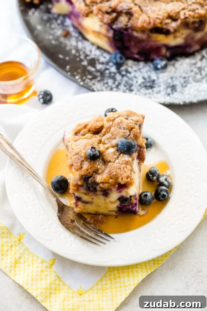 3 Irresistible Instant Pot Blueberry French Toast Bakes 6 Fresh blueberries adorn a slice of French toast bake, accompanied by a drizzle of maple syrup and a dusting of powdered sugar. A vintage fork rests on a white lace plate, with a bottle of maple syrup in the background, completing a delightful breakfast or brunch scene.