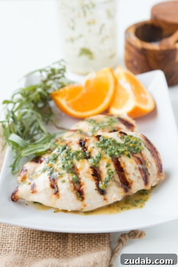 Grilled Orange Tarragon Chicken for a light but totally flavorful dinner. Perfectly grilled orange tarragon chicken breast, garnished with fresh tarragon sprigs and orange zest, on a rustic wooden board.