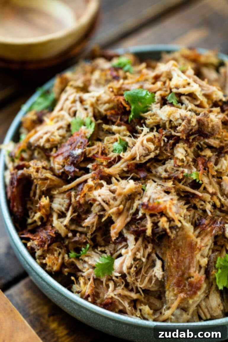 Crockpot Carnitas: Crispy & Juicy Pulled Pork 5 A close-up view of a bowl overflowing with tender, shredded pork carnitas, beautifully topped with a generous sprinkle of fresh cilantro and accompanied by bright lime wedges.