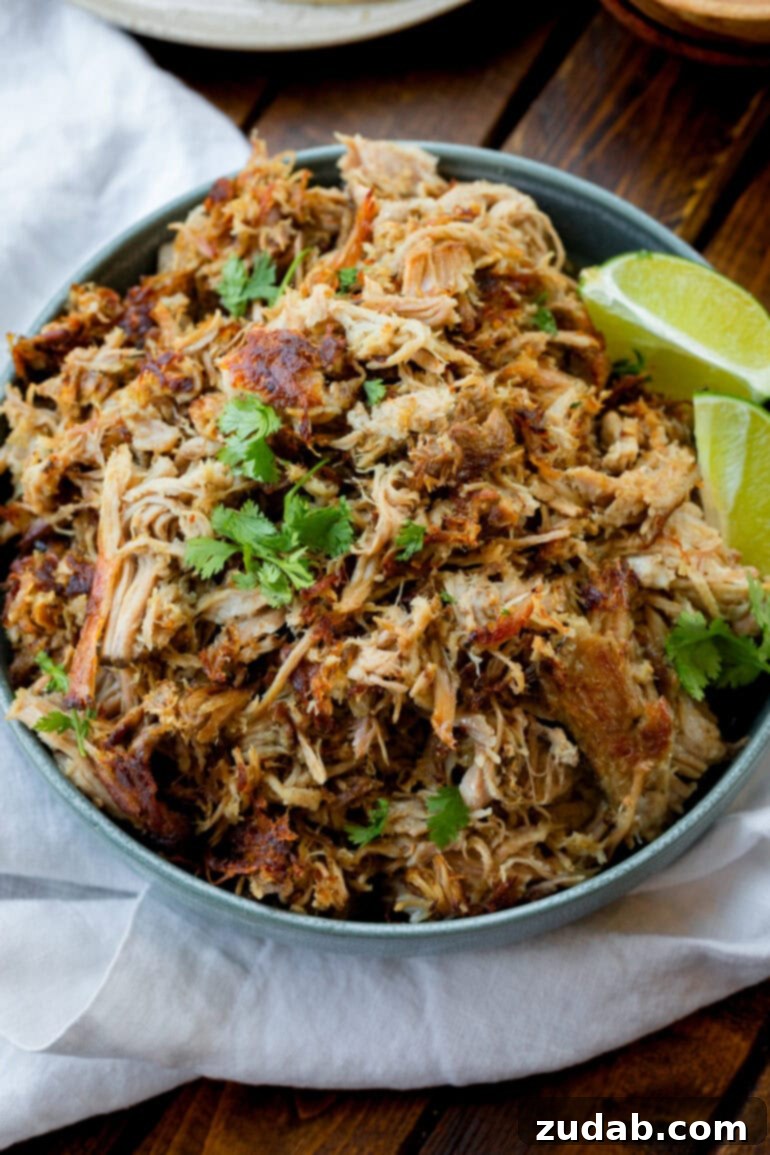 Crockpot Carnitas: Crispy & Juicy Pulled Pork 8 A beautiful bowl of shredded pork carnitas, generously topped with fresh cilantro, and served with a side of vibrant lime wedges for a burst of citrus flavor.