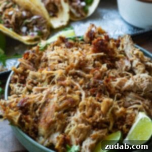 A mouthwatering photo of shredded pork carnitas in a bowl, ready to be served, with tacos in the background.
