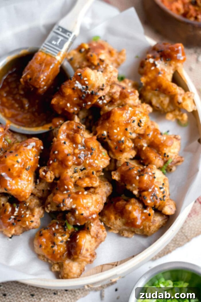 Crispy Korean Fried Chicken 7 A close-up of a single piece of Korean Style Fried Chicken, coated in sticky red sauce and topped with fresh scallions and sesame seeds, highlighting its crispy texture.