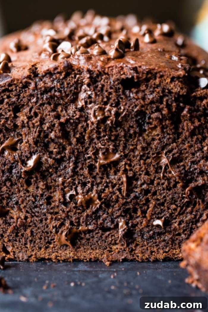 Ultimate Double Chocolate Banana Bread 4 A beautifully baked loaf of chocolate banana bread with a single slice cut, revealing a dense, moist interior generously packed with melted chocolate chips.